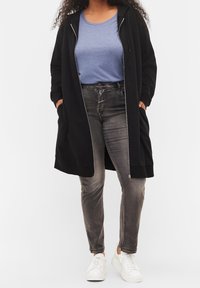 Sudadera con cremallera negra y bolsillos sobre una camiseta azul, combinada con jeans grises y zapatillas blancas. El tejido parece suave y casual.