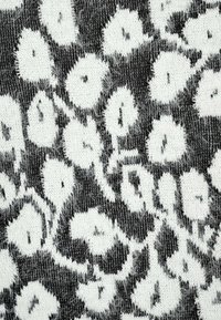 Schwarz-weißes, flauschiges Strickgewebe mit einem abstrakten Blumenmuster, das kreisförmige Formen und blattartige Details zeigt.