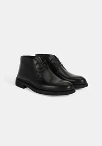 Bottines en cuir noir avec une texture lisse, bout arrondi et design à lacets. Présente une couture minimale et une semelle en caoutchouc noir robuste.