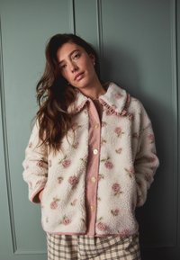 Faux fur jakke med blomstermønster i off-white og pink, med knaplukning og en flæsekantet krave. Stylet med en pink top og ternede bukser.