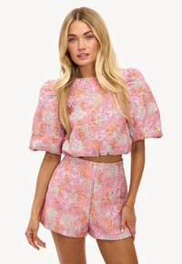 Crop top floral rose avec des manches bouffantes et un short taille haute assorti, présentant un tissu texturé avec des accents orange et bleu.