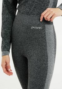 Šedé legíny s vzorovanou boční částí, vyrobené z elastického materiálu, s bílým nápisem "protest" na pase.