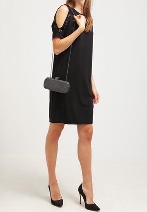Černé šaty s odkrytými rameny, krátké rukávy, hladká tkanina, volný střih. V kombinaci s texturovanou černou kabelkou a vysokými podpatky.