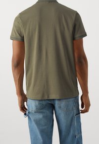 Olivgrön kortärmad polo med en texturerad krage och fåll. Bärs med ljusblå denimbyxor med sidofickor.