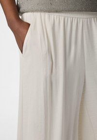 Pantaloni beige a gamba larga con una texture leggera e liscia, dotati di tasche laterali e una vita elastica per il massimo comfort.