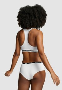 Weißer Sport-BH und passende Unterwäsche mit schwarzen Logo-Bändern, im Racerback-Design und mit glatter Textur, von hinten betrachtet.