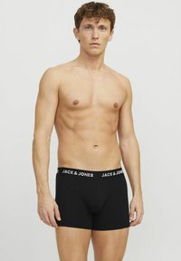 Fekete boxer alsónadrágok láthatóak egy logózott derékrésszel, férfi modellen. Az alsónadrágok szoros fazonúak és sima szövettextúrával rendelkeznek.