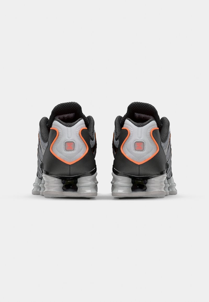 Baskets de sport noires et grises avec un dessus texturé et des accents orange. Équipées d'une épaisse semelle transparente avec un soutien rembourré au niveau du talon.