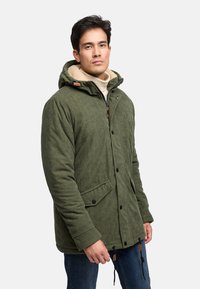 Grüne Cordjacke mit Kapuze, Frontknopfverschluss, zwei seitlichen Taschen und Kordelzügen am Saum. Gefütterter Kragen in einem kontrastierenden Beige.