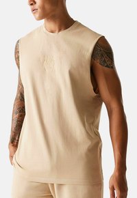 Canotta in cotone beige senza maniche con un ricamo discreto del logo di un toro al centro del petto, dal taglio comodo e dalla texture liscia.