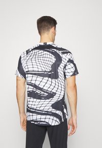 Koszulka z krótkim rękawem z czarno-białym abstrakcyjnym wzorem w siatkę, wykonana z lekkiego materiału, z okrągłym dołem i logo Nike na szyi.
