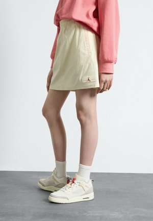 Shorts de sport jaune clair avec une taille élastique, des poches latérales et un petit logo brodé en bas à gauche. Sweat-shirt rose décontracté et baskets.