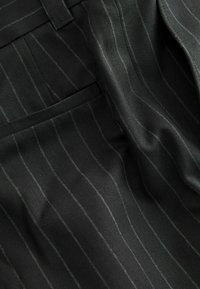 Black pinstripe fabric with a herringbone texture, featuring fine white stripes and soft draping. Includes a pocket and tailored finish.