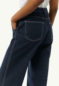 Donkerblauwe denim jeans met een hoge taille, voorzien van contrasterende witte stiksels en twee achterzakken. Gladde textuur, wijde pijpen.