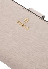Portfel Furla w miękkiej różowej teksturowanej skórze z złotym logo. Charakteryzuje się kompaktowym designem z zapięciem na klapkę i smukłym profilem.