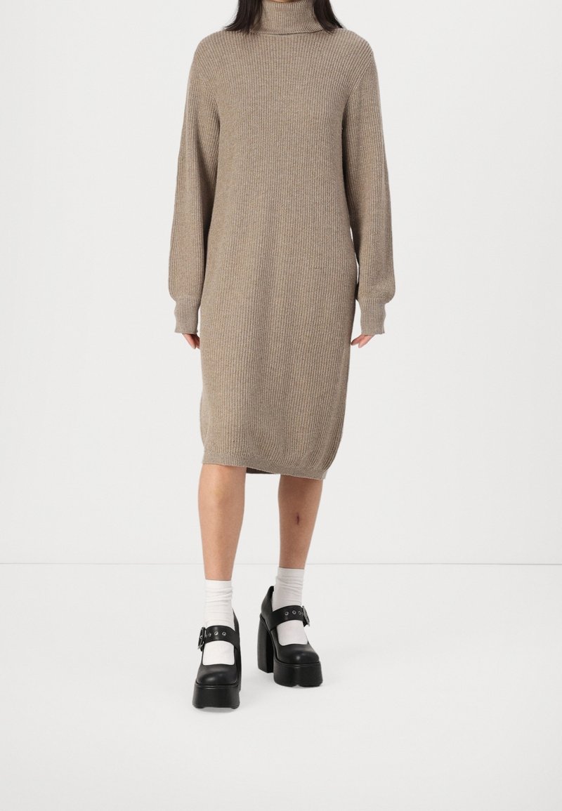 Personne portant une robe midi beige en maille à col roulé avec manches longues, chaussettes blanches et chaussures Mary Jane à plateforme noires.