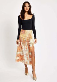 Black long-sleeve top paired with a cream skirt featuring an orange paisley pattern and a side slit, complemented by gold heels.