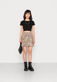 Top cropped preto com riscas e mangas curtas, saia mini plissada em tons de bege e castanho, mala preta texturizada e botas pretas de cano alto com fivelas.