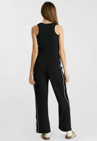 Zwarte geribbelde tanktop gecombineerd met zwarte wijde broek met witte zijkanten. De outfit heeft een relaxte pasvorm en eenvoudige ontwerpelementen.