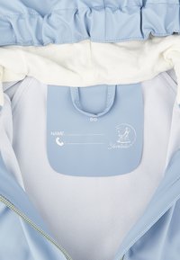 Helles blaues Jackeninnenteil mit geripptem weißen Futter. Verfügt über eine Namensschildtasche und ein gedrucktes Logo. Glattes Material mit Reißverschluss.