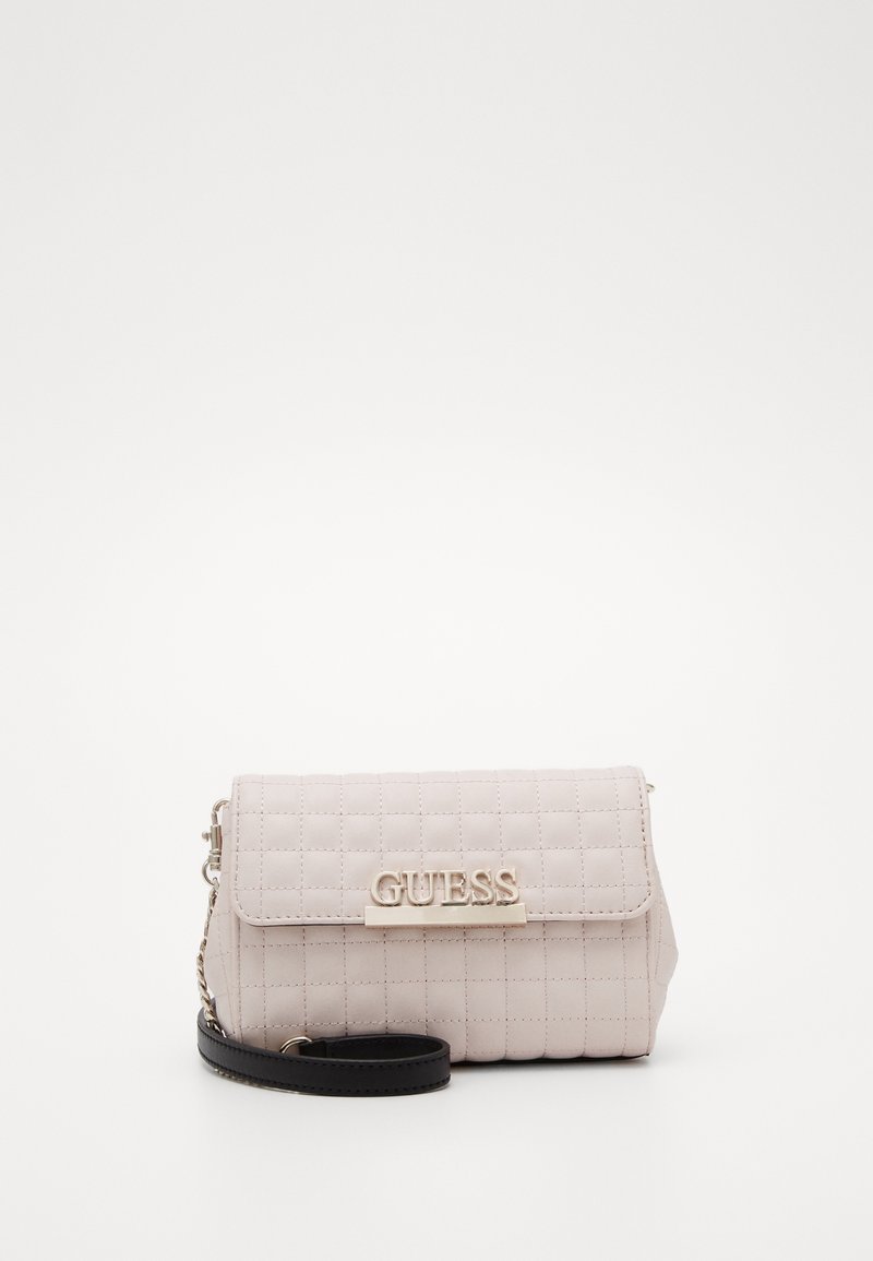 Pochette bracelet matelassée beige clair avec logo "GUESS" argenté et lanière noire sur fond blanc.