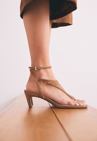 Sandales à talons en daim marron avec un design à brides, une boucle à la cheville et un bout ouvert. Caractéristiques : talon léger et semelle plate.