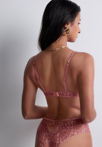 Soutien-gorge en dentelle et culottes assorties en rose doux, présentant des motifs raffinés, des bretelles réglables et des accents en métal doré.