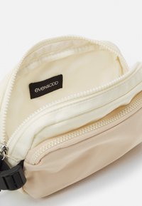 Borsa di stoffa morbida in crema e beige con chiusura a zip; presenta un'etichetta interna e un materiale testurizzato in contrasto alla base.