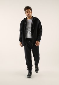 Must musta lukuga dressipluus, millel on nöör. Selle toeteks mustad vabaaja püksid. Lihtne disain, tehtud pehmest kangast, pakub lõdvestunud istuvust ning taskuid.