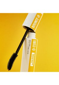 Tube de mascara Maybelline en blanc et jaune, avec une prise texturée, un applicateur noir et une étiquette audacieuse indiquant "COLLOSAL CURL" et "BOUNCE."