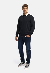 Svart genser med hvit krage, kombinert med mørkeblå jeans og flerfargede joggesko. Genseren har en knappet halslinning og ribbede mansjetter.