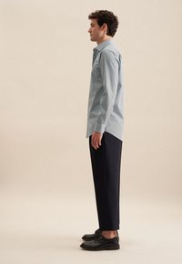Camicia button-up a righe azzurre e bianche, maniche lunghe, abbinata a pantaloni scuri e scarpe nere. Tessuto morbido, design del colletto classico.