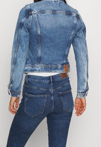 Jeansjacka i ljusblått med blekt mönster och knappstängning; har en märkesetikett på baksidan. Matchad med mörkblå skinny jeans.