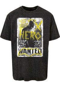 Camiseta gráfica negra con un diseño estilo cómic, que incluye una figura de superhéroe, texto en amarillo brillante y una textura envejecida.