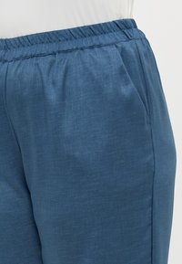 Blå byxor i texturerat tyg, med resårmidja och sidofickor, samt en något avsmalnande benform.