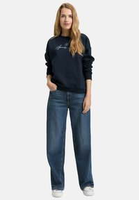 Navy sweatshirt with a light blue embroidered design, paired with wide-leg blue denim jeans and white sneakers. Smooth fabric and casual fit.