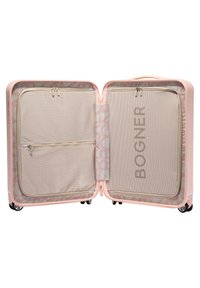 Valigia rigida rosa aperta, con tasche in rete e interno beige con logo BOGNER. Visibili ruote lisce e scomparti con zip.
