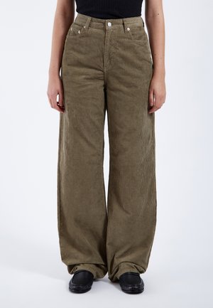 Olivenfarvede kordfløjspants med brede ben, lodret ribbing, forlommer og knaplukning. Sammen med sorte slip-on sko.
