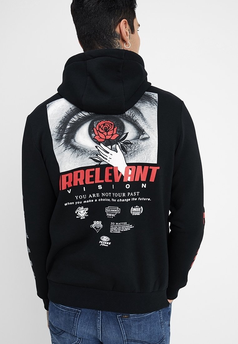 Personne portant un sweat à capuche noir avec un grand graphisme d’un œil, une rose rouge et une main, ainsi que le texte en gras « IRRELEVANT » et des phrases motivantes.