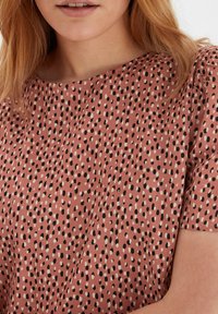 Top in tessuto rosa con scollatura rotonda, caratterizzato da un motivo a pois nero e crema. Texture liscia e maniche corte.