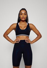 Sutiã desportivo preto com listas brancas sob o busto e calções de cintura alta coordenados. Textura suave, design ajustado e detalhes minimalistas.