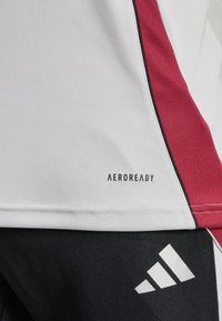 White athletic shirt with red and black side accents, featuring "AEROREADY" logo at the hem. Soft, smooth fabric texture.