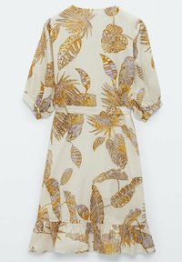 Robe à manches courtes avec un motif floral sur fond beige, présentant des feuilles tropicales aux teintes dorées et violettes, avec un ourlet volanté.