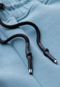 Jasnoniebieska tkanina o gładkiej strukturze z czarnymi sznurkami ściągającymi. Sznurki mają gumowe końcówki z metalowymi końcami dla większej trwałości.