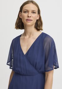Marinblå, lätt klänning med omslagdesign, djup V-ringning och genomskinliga skjortärmar; slät yta och enkel elegans.
