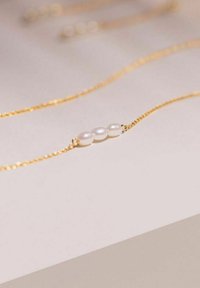 Collar de cadena de oro con tres perlas iridiscentes, con un diseño delicado y una textura suave, dispuestas en una línea horizontal.