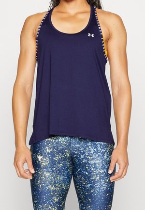 Atletisk person iført en marineblå Under Armour tank top med logo og blå spraglede træningsleggings med gul og hvid sprøjtet mønster.