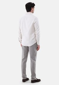 Weißes Langarmhemd mit Knöpfen, kombiniert mit hellgrauen Hosen. Das Outfit wird mit dunkelbraunen Schuhen und einem lockeren Schnitt abgerundet.