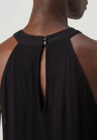 Musta hihaton mekko, jossa on korkea kaulus, takana halkio ja kaksi nappia kiinnitykselle. Valmistettu kevyestä, teksturoidusta kankaasta.