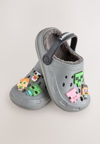 Sabots en mousse gris avec une doublure douce et brune en fausse fourrure. Comprend cinq breloques de personnages pixélisées colorées attachées à la bride noire réglable supérieure.